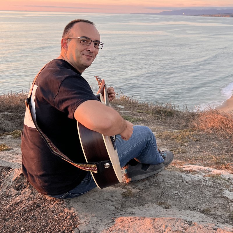 Atti, playing an acoustic guitar on the coast at sunset